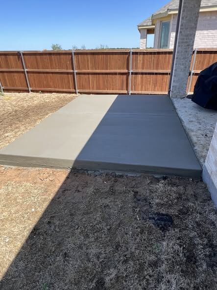 Freshly poured and finished concrete patio slab along a backyard fence
